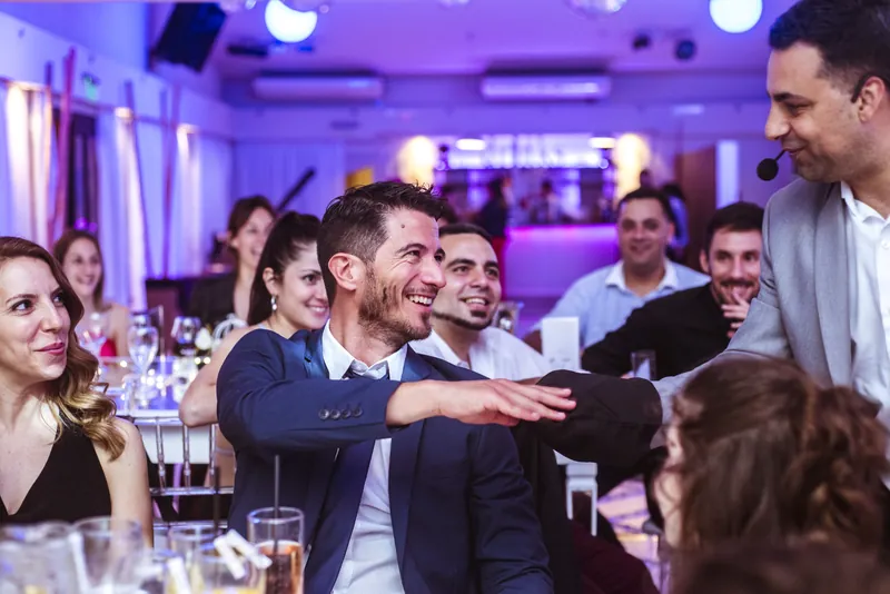 Invitados de un casamiento muertos de risa en la mesa mientras Komodín hace un truco