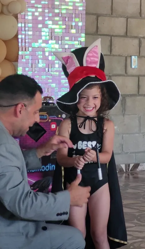 Una nena con galera de orejas de conejo y capa de mago